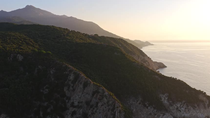 A stunning aerial ascent reveals the dramatic green cliffs and mountains along the coastline during a beautiful sunrise