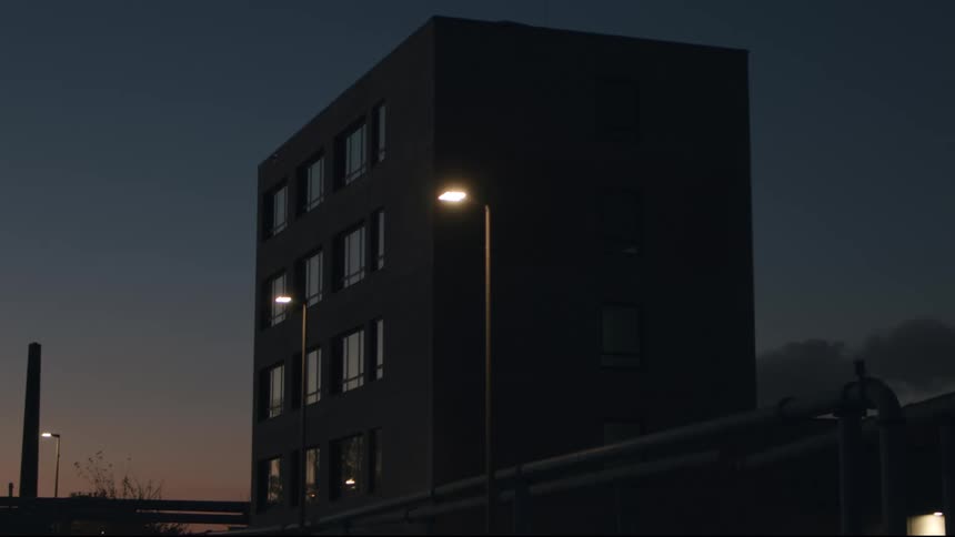 A contemporary industrial building stands silently under streetlights against a beautiful twilight sky