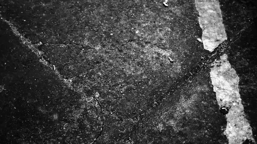 A gritty, black and white, top-down view of cracked asphalt with a faded white line