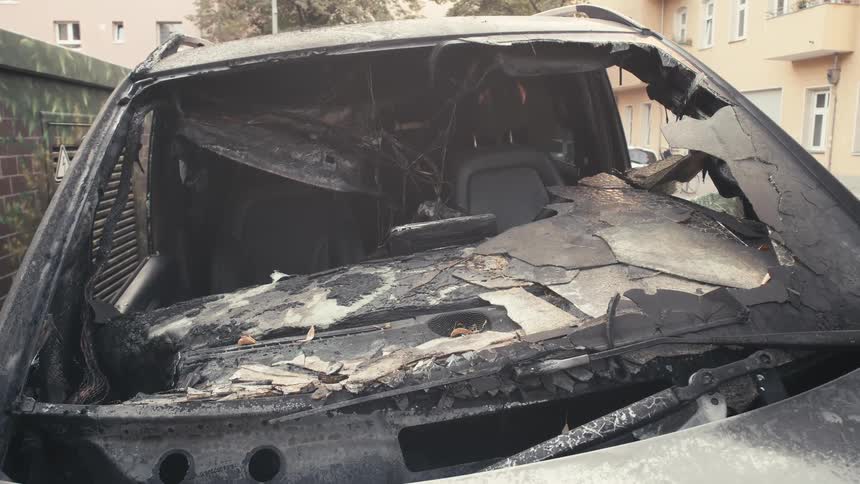 A static shot of a burnt-out car's front windshield and dashboard on a city street