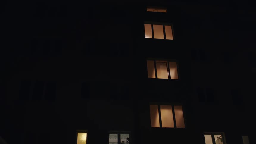 Warm lights glow from the windows of a dark apartment building on a still night
