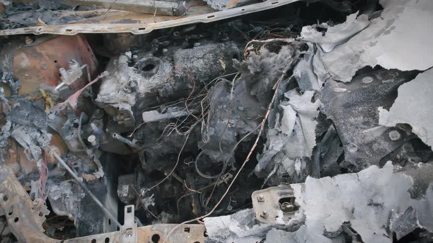 A close-up view reveals the charred and destroyed engine of a car after a devastating fire