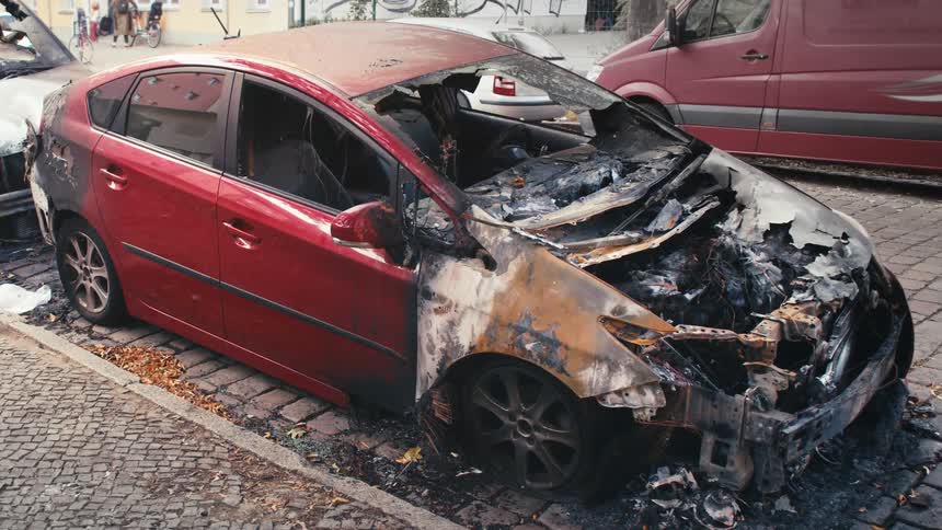 The charred and melted remains of a red car sit on a city street after being destroyed by fire