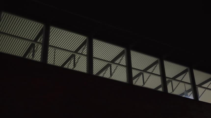A low angle static shot of illuminated windows on an industrial building at night