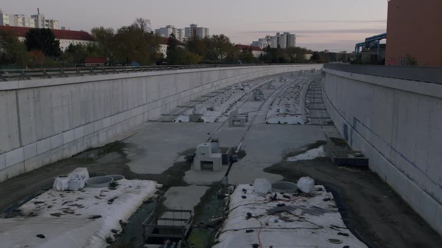Wide static shot of a large, empty railway construction site within a concrete trench during twilight