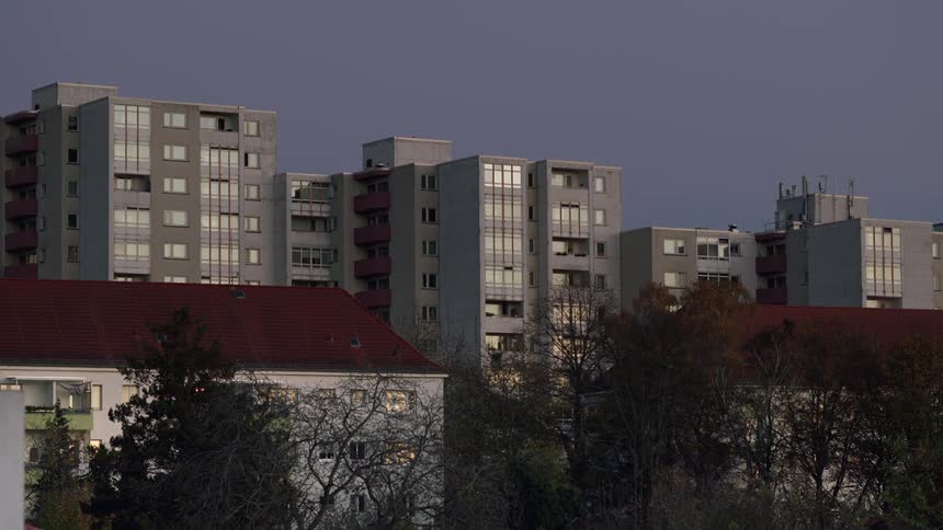 A still shot of large residential apartment buildings at dusk with lights turning on in the windows