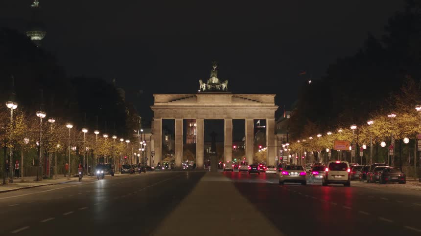 Busy city traffic flows down the illuminated boulevard towards the iconic Brandenburg Gate at night in Berlin, Germany