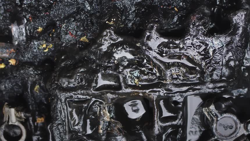 A macro close-up shot of thick, black, oily liquid slowly dripping over a dark, textured, and abstract industrial surface