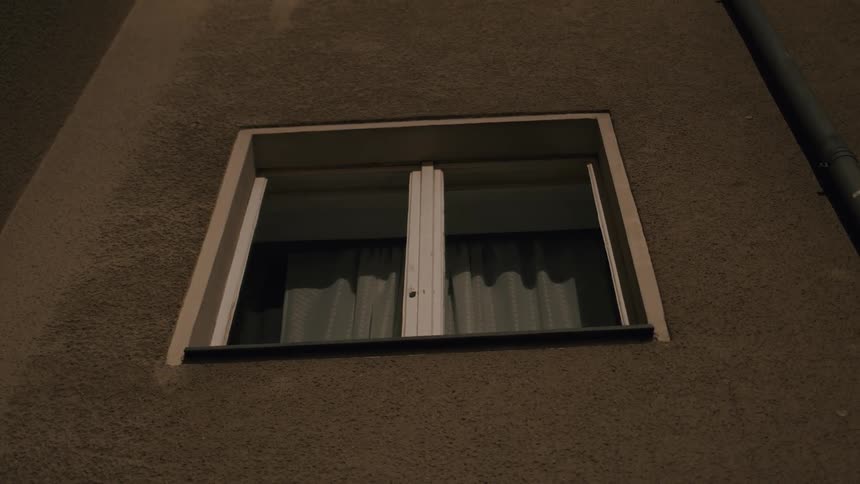 A static shot of a residential building's window as seen from the outside at night