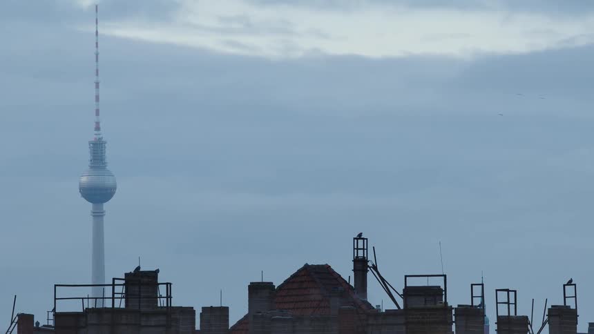 The Berlin TV Tower, Fernsehturm, stands tall over city rooftops on a gloomy, overcast day