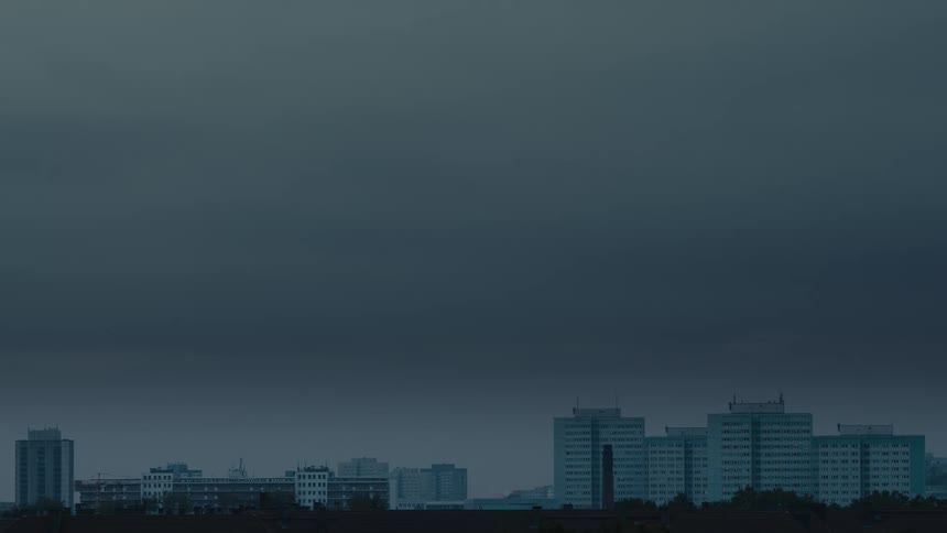 A bleak city skyline with apartment blocks sits under a dark, foreboding sky