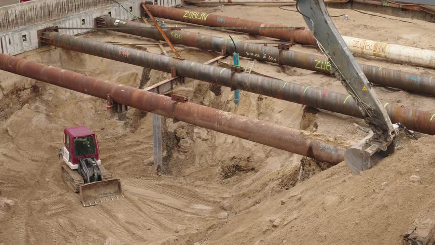 A high-angle view of a large construction excavation pit with heavy machinery and massive steel support pipes