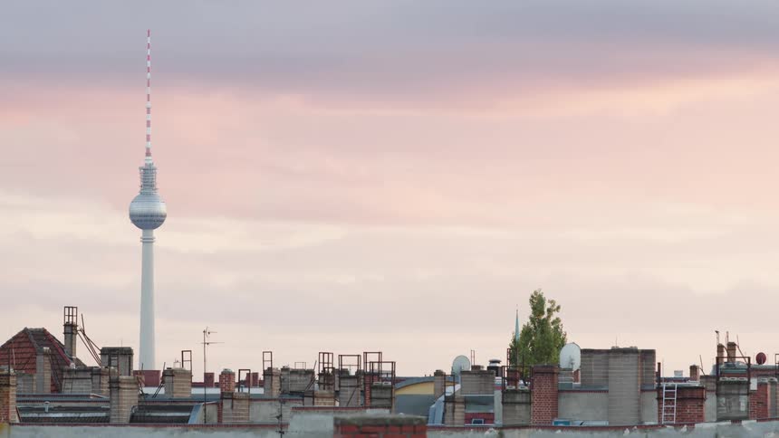 The Berlin TV Tower stands tall over city rooftops against a beautiful pink sky at sunrise