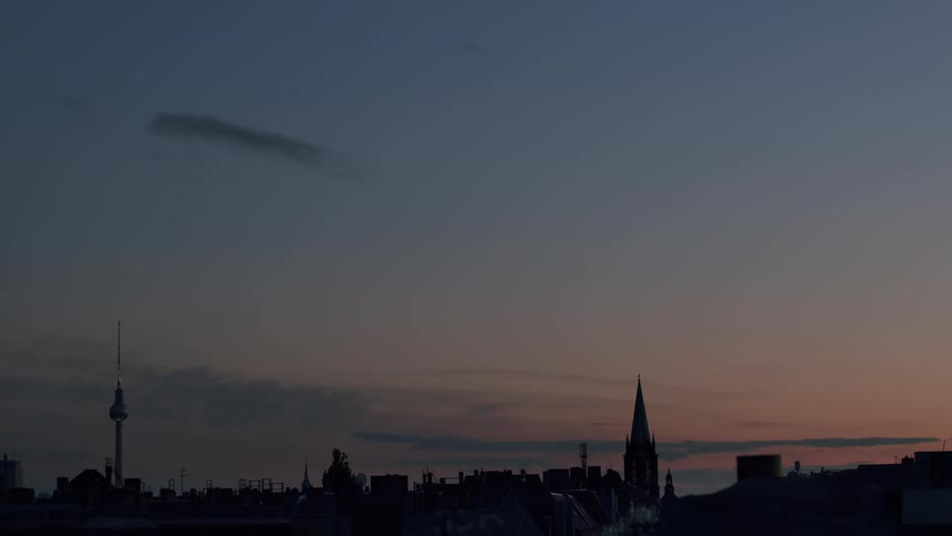 A serene, static view of the Berlin city skyline with the iconic TV tower and a church steeple silhouetted against a colorful dusk sky