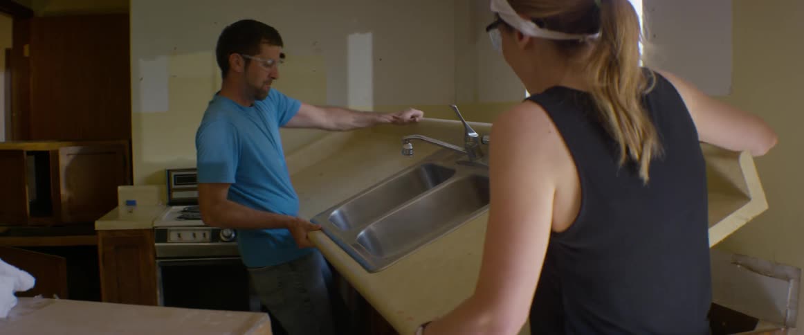 A man and woman lift up and carry away a kitchen countertop and sink