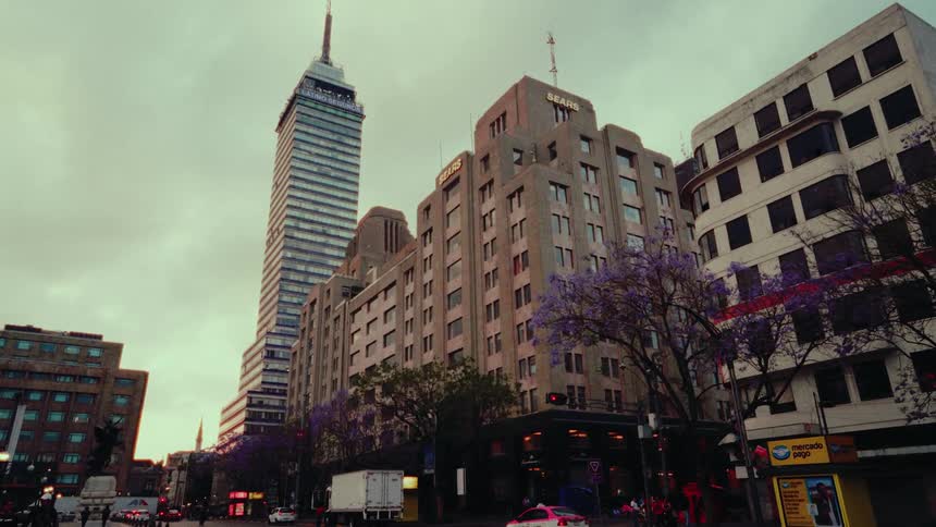 The iconic Torre Latinoamericana skyscraper towers over a bustling Mexico City street corner on a cloudy day