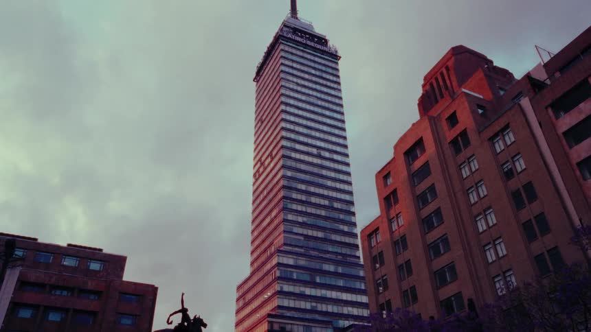A dramatic low-angle shot slowly zooms in on the iconic Torre Latinoamericana skyscraper in Mexico City against a moody, cloudy sunset sky