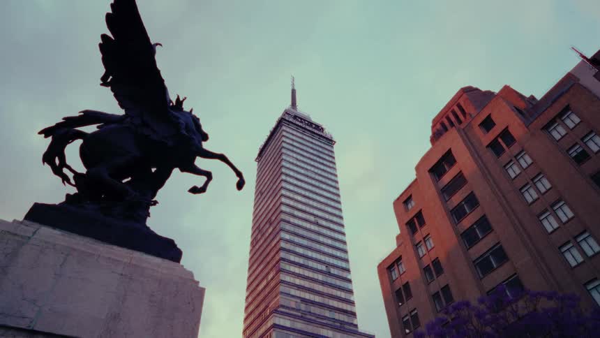 A cinematic low-angle shot reveals the iconic Torre Latinoamericana skyscraper and a silhouetted winged horse statue against the dusk sky in Mexico City