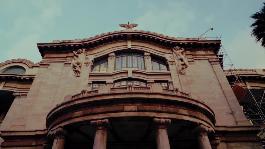 A low-angle view slowly tilts up the grand, ornate facade of a historic classical building under a clear sky