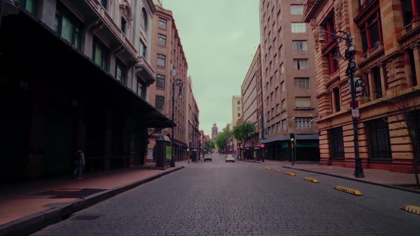 A lone pedestrian walks along the sidewalk of a nearly deserted cobblestone street in a historic city center on an overcast day