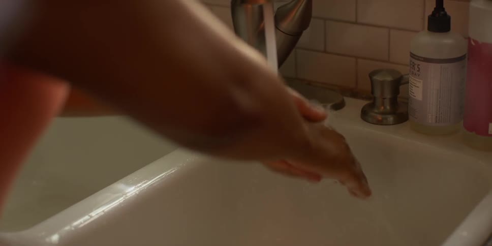 A woman washes her hands at the kitchen sink