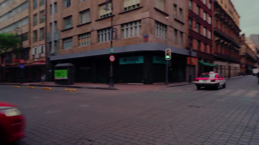 A classic pink and white CDMX taxi drives through a quiet intersection on a historic cobblestone street in Mexico City