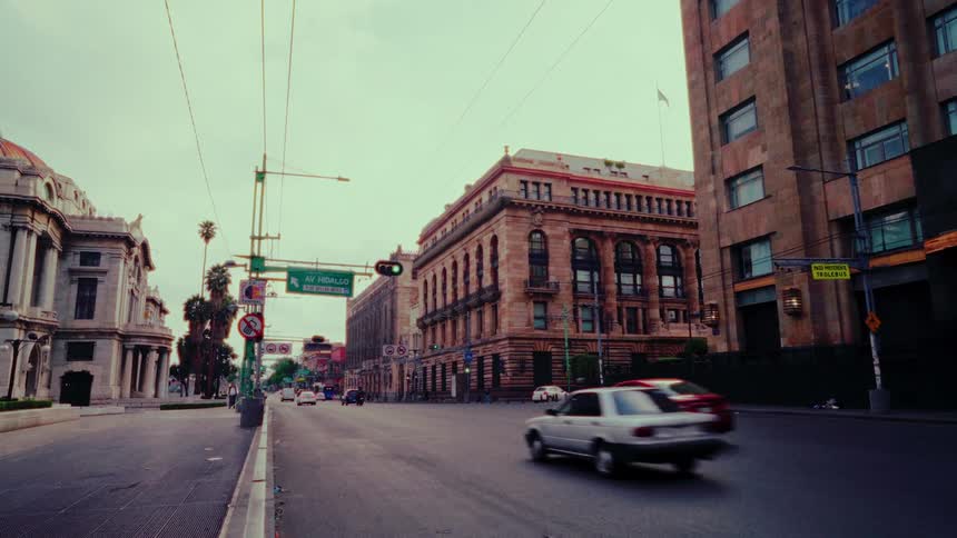 Traffic flows along a historic city street in Mexico City on an overcast day
