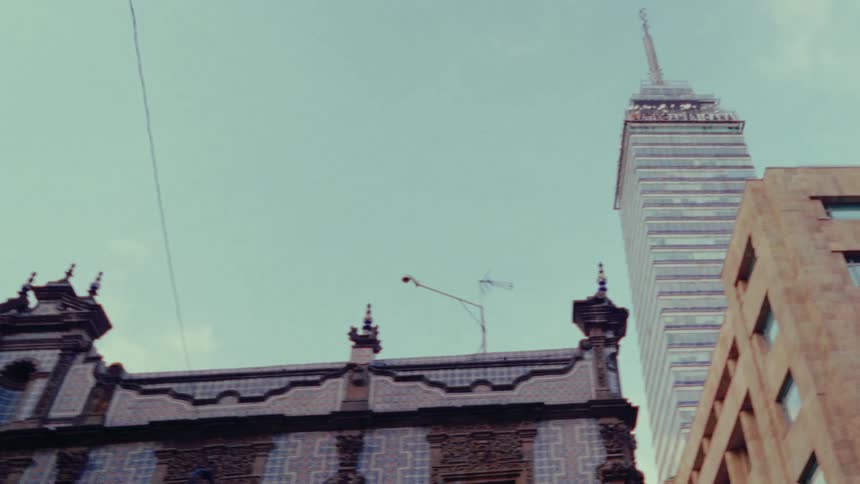 A low-angle pan across historic and modern buildings reveals the iconic Torre Latinoamericana skyscraper against a clear sky in Mexico City