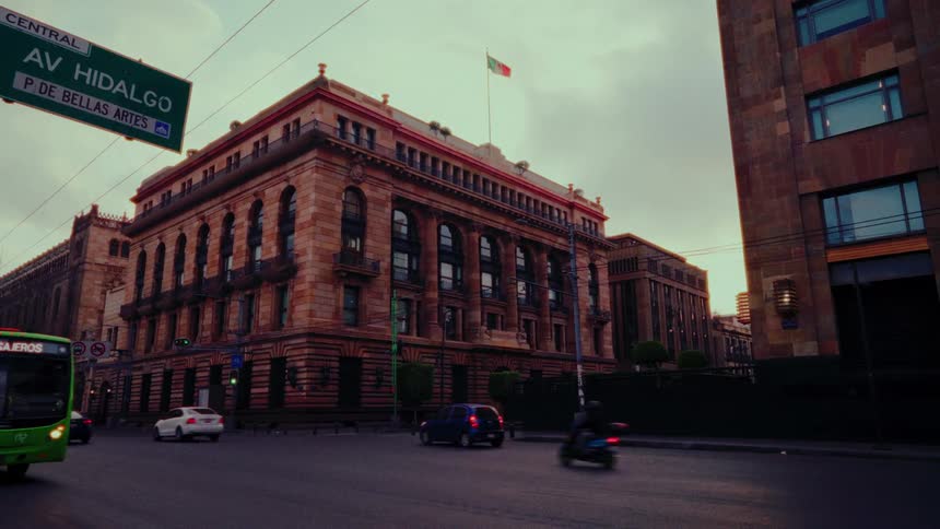 Traffic flows past a historic building on Avenida Hidalgo near the Palacio de Bellas Artes in Mexico City at dusk