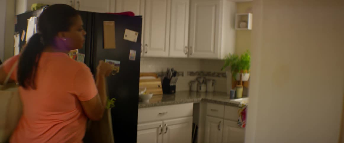 A woman walks into the kitchen with bags