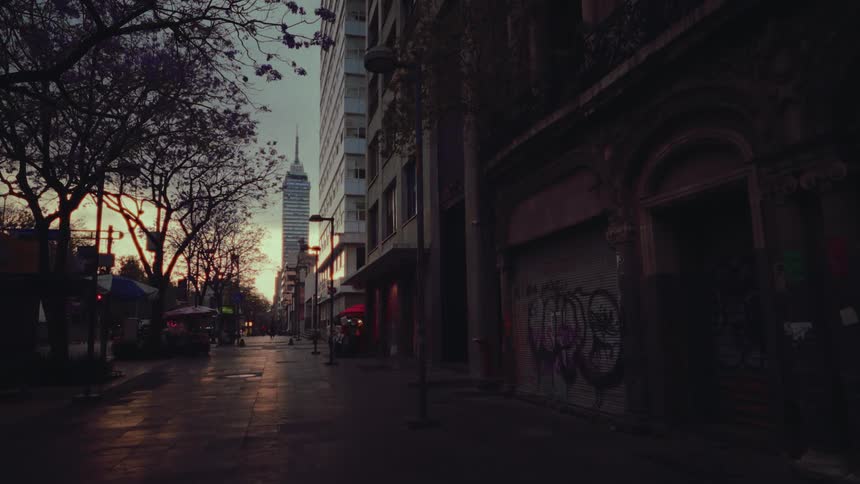 A delivery cyclist rides down a moody street in Mexico City at sunset with the Torre Latinoamericana in the background