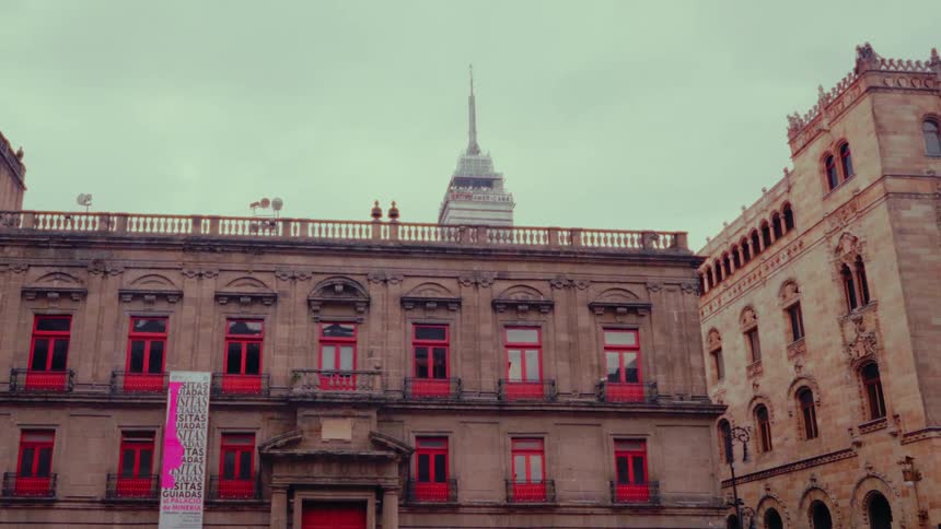 The modern Torre Latinoamericana rises behind the historic National Museum of Art with its striking red windows on a cloudy day in Mexico City