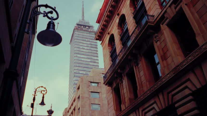 A slow dolly shot looks up from a city street at the Torre Latinoamericana skyscraper framed by historic architecture