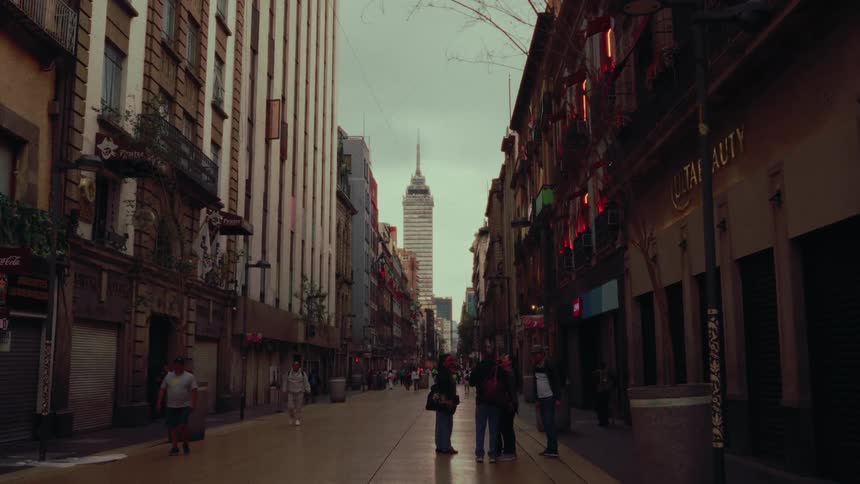 A slow push-in shot down a historic pedestrian street in Mexico City frames the iconic Torre Latinoamericana against an overcast sky