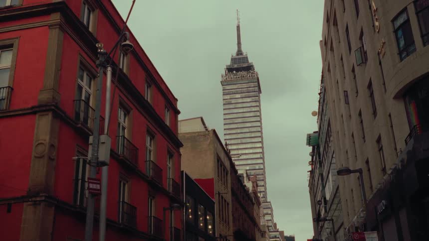 A slow zoom-in shot captures the iconic Torre Latinoamericana skyscraper looming over the historic streets of Mexico City on an overcast day