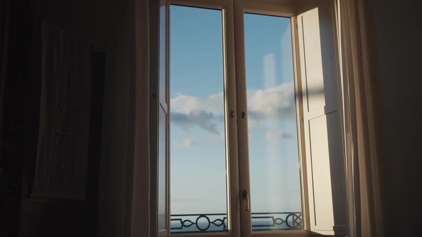 Sunlight illuminates an open window looking out over a calm blue sky and ocean