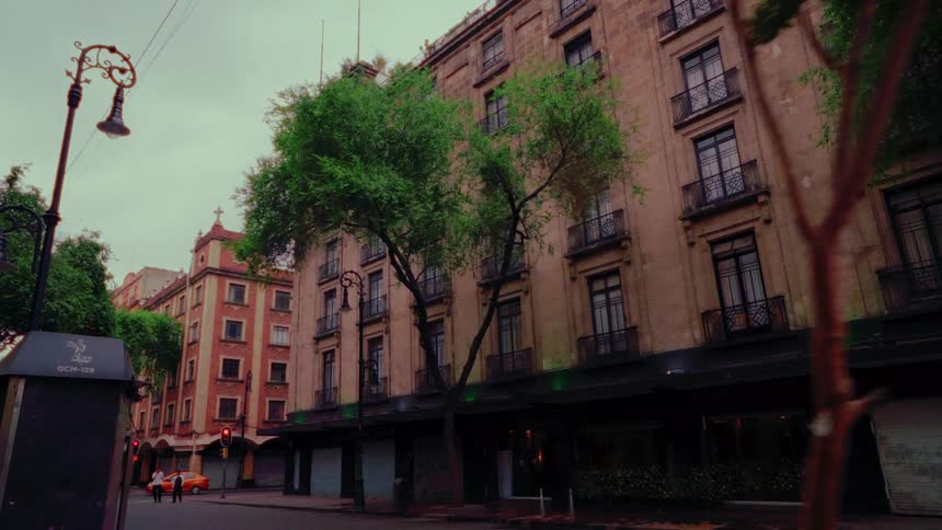 A slow, moody dolly shot towards a historic building on a quiet, tree-lined street in Mexico City on a cloudy day