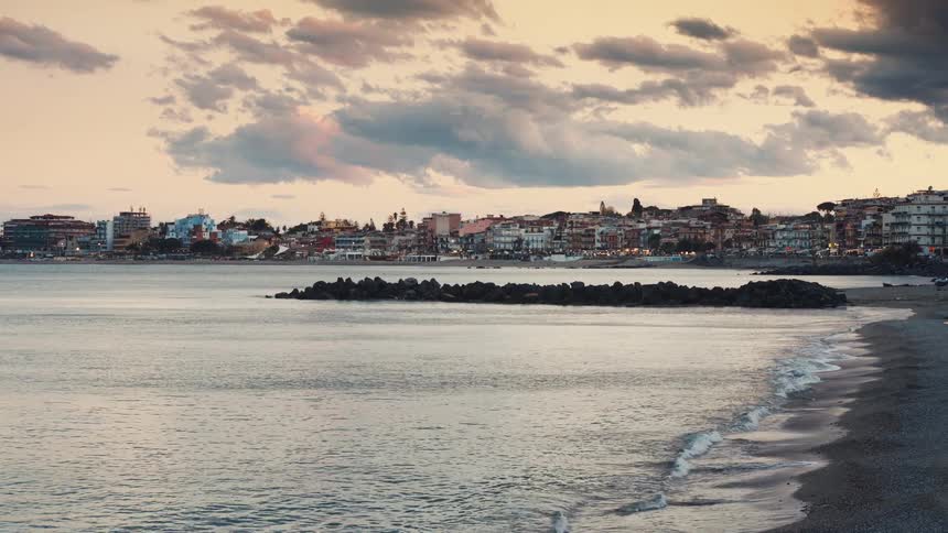 Gentle waves lap the shore of a beautiful coastal town at dusk under a cloudy sky