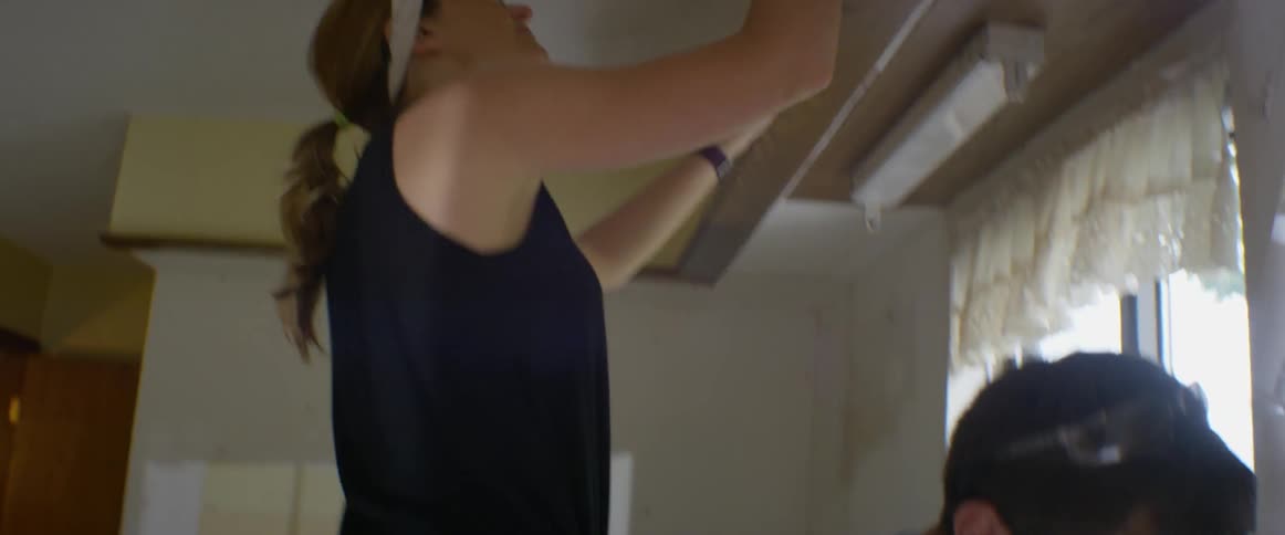 A woman rips wallpaper, man works on electrical outlet