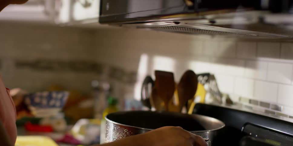 A woman adds ingredients to a cooking pot on the stove