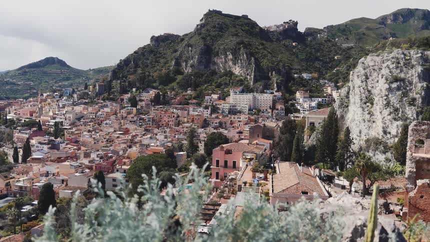 A stunning panoramic view of the picturesque town of Taormina, Sicily, nestled in the green, rocky mountains of Italy
