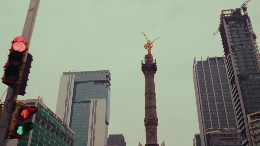 A slow dolly shot reveals the Angel of Independence monument standing tall amidst the modern skyscrapers of Mexico City
