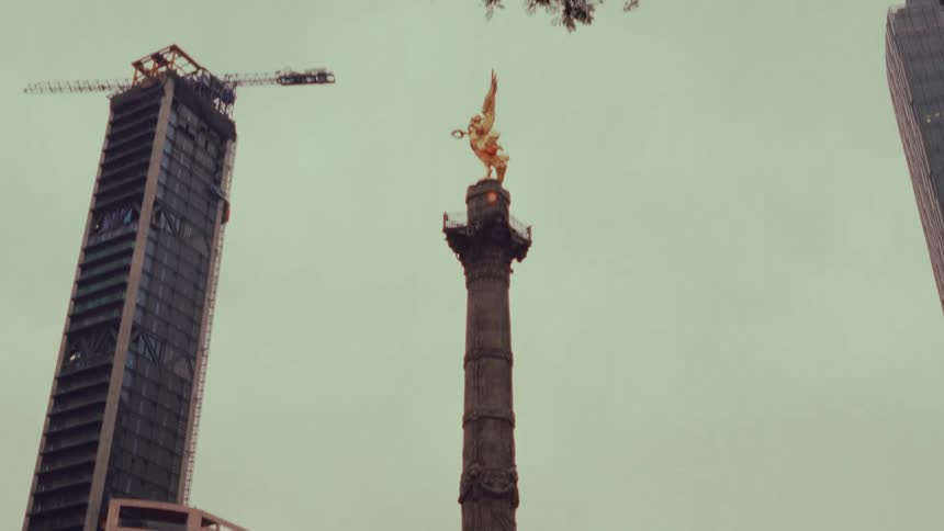 A tilt-up shot of the iconic Angel of Independence in Mexico City, starting with the crowds gathered at its base and revealing the golden statue against a modern skyline