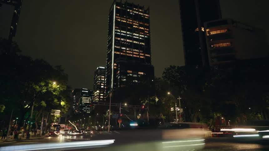 A dynamic night time-lapse captures streaks of traffic light on a bustling city street below towering modern skyscrapers with police cars present