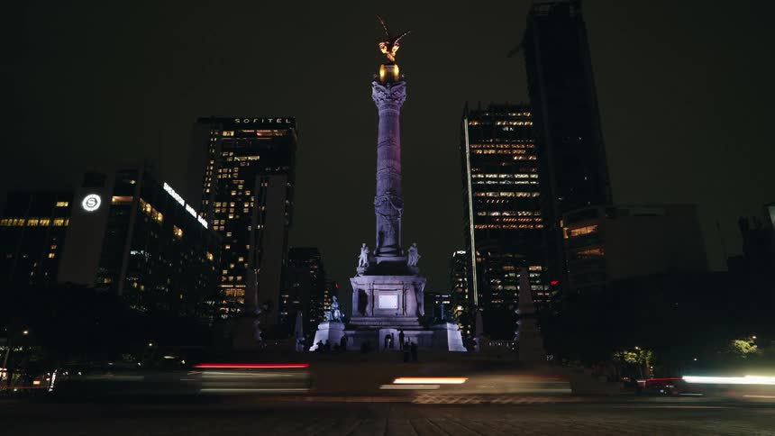 Nighttime time-lapse of traffic creating light trails around the iconic Angel of Independence monument in Mexico City