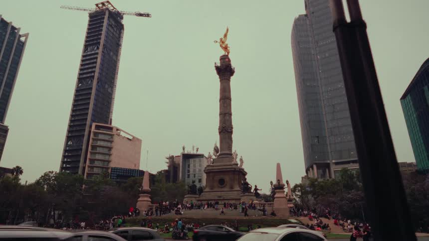 The iconic Angel of Independence monument stands tall in a busy Mexico City roundabout, surrounded by modern skyscrapers and bustling traffic