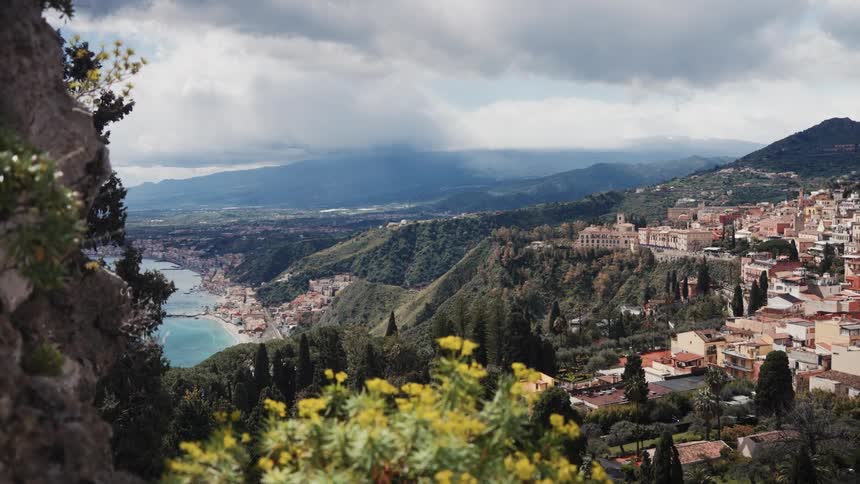 A scenic high-angle view of a beautiful coastal town nestled in the green hillsides overlooking the sea under a dramatic cloudy sky
