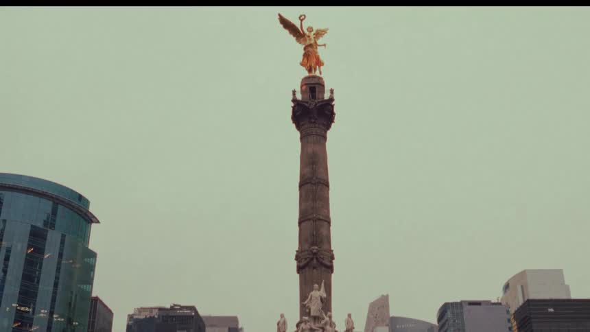 A slow camera tilt up reveals the iconic Angel of Independence monument in Mexico City, with crowds of people gathered at its base