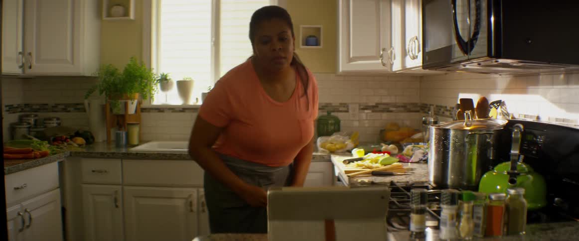 A woman is cutting food and walks over to a tablet