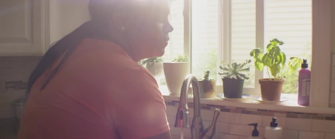 A woman washes her hands at a kitchen sink